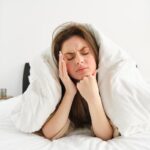 portrait woman rolled blankets bed frowning feeling unwell has hangover headache 1 Common Sleep Problems Caused by the Wrong Mattress